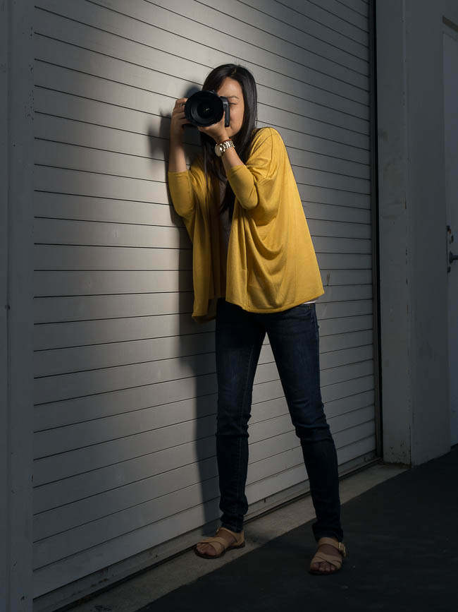 Photographer bracing against a wall while holding camera demonstrating how to use a stable surface as an anchor for slow shutter speed shooting