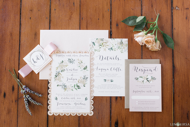 Wedding invitation suite detail shot arranged as a flatlay on a white linen surface with rings and a flower included in the composition